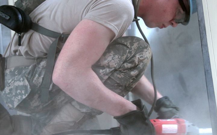 Worker in ear protection kneeling to grind a concrete floor